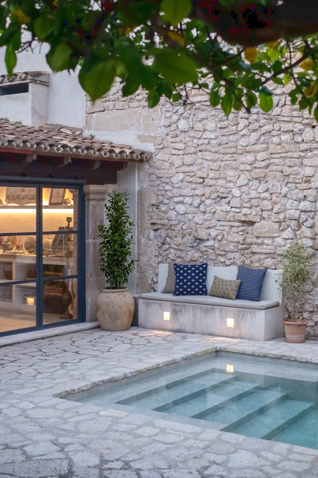 Terraza con piscina, muro de piedra y banco con cojines en Can Costa